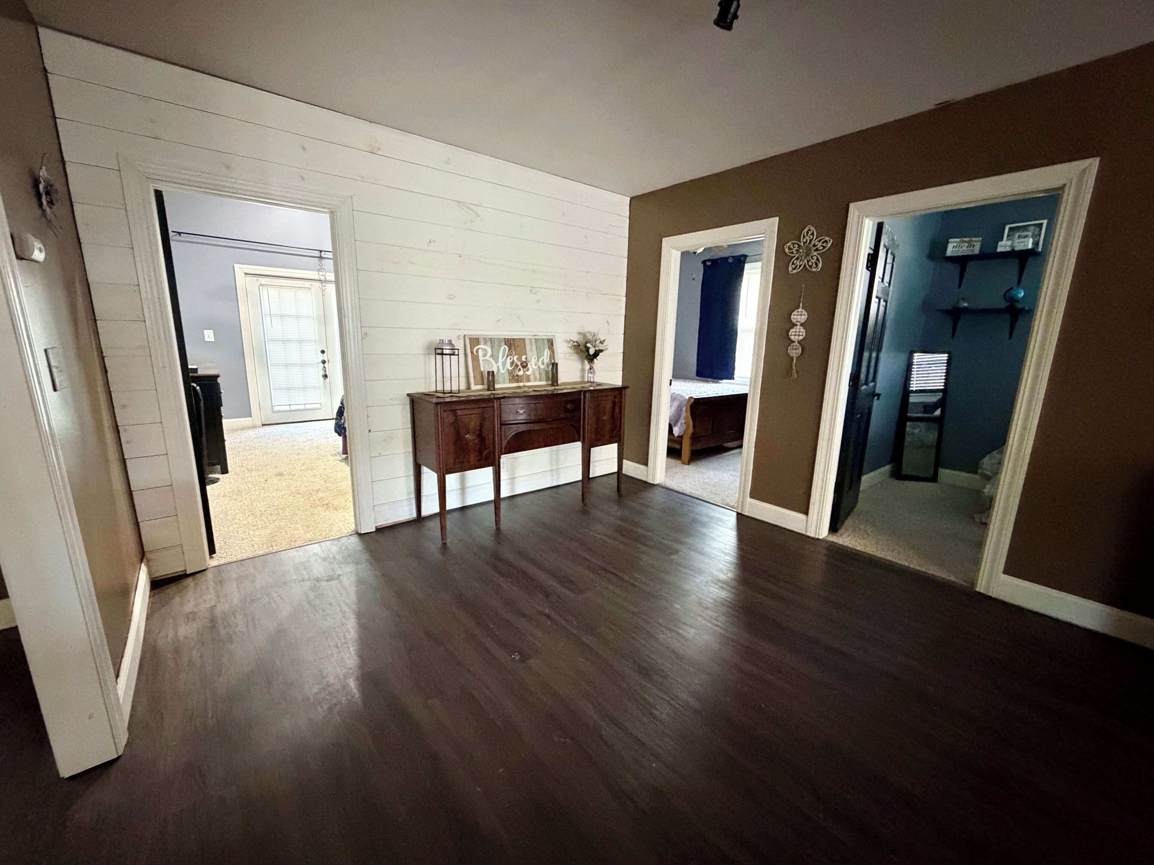 Une pièce avec un plancher en bois, un bureau sur lequel est posé un panneau, et une porte qui donne sur une autre pièce.