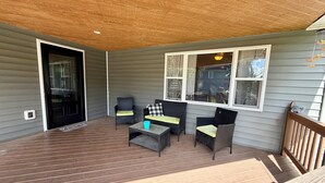 A covered porch with a wooden deck, wicker furniture, and a view of the neighborhood.