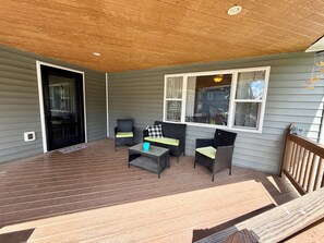 A covered porch with a wooden deck, wicker furniture, and a view of the neighborhood.