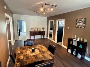 A dining area with a wooden table and chairs, a chandelier, and a wall sign.