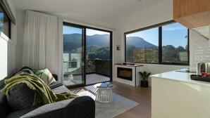 A modern living room with a sofa, a small round table, and a view of mountains through large windows. - Mosswood - Breath Quiet Hideaways, Hobart (Fern Tree)