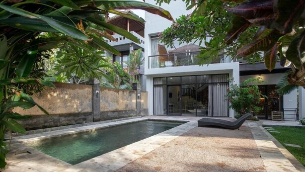 Una casa moderna con piscina, un patio cubierto y abundante vegetación.