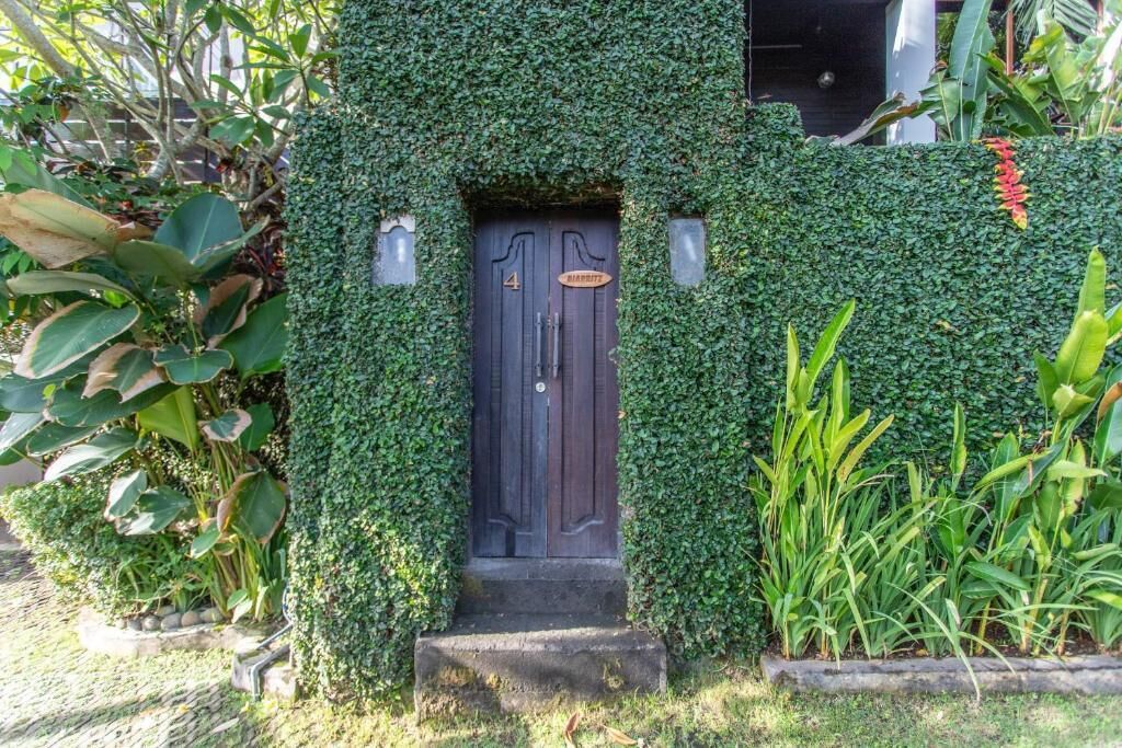 A dark wooden door with a sign above it, surrounded by lush green foliage.