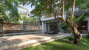 Un espacio exterior moderno con piscina, sillones de descanso y un árbol.