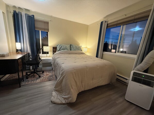 Un dormitorio con cama, escritorio, silla y aire acondicionado.