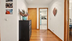 Un corridoio con pavimento in legno, un comò nero e un vaso con fiori secchi. In parete, tre quadri incorniciati.
