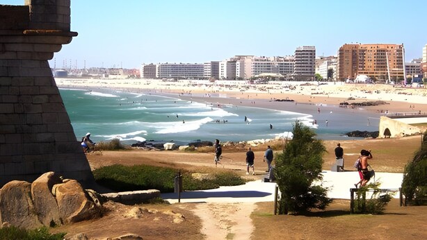Vista sulla costa con un faro, una spiaggia e edifici sullo sfondo.