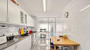 Una cucina con mobili bianchi, un tavolo di legno e un orologio appeso al muro.