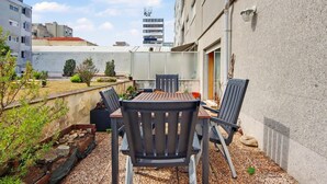 Patio esterno con tavolo e sedie, un piccolo giardino e vista sugli edifici circostanti.