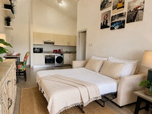 Ein Schlafzimmer mit Bett, Nachttisch, Lampe und Blick auf die Küche.