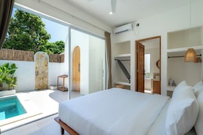 Ein Schlafzimmer mit einem großen Bett, einem kleinen Tisch, einem Stuhl, einer Einbauschränke und einer Schiebetür, die auf einen Balkon mit Pool führt.