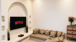 Ein Wohnzimmer mit flachbildfernseher an einer weißen Wand, einem beigen Sofa und einer Holzkommode.