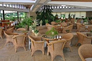 An indoor patio area with wicker furniture, potted plants, and a view of the outdoors. - Hotel Imperial - Riviera Holiday Club Varna (Varna)