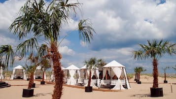 Um resort no deserto com palmeiras, tendas brancas e solo arenoso.