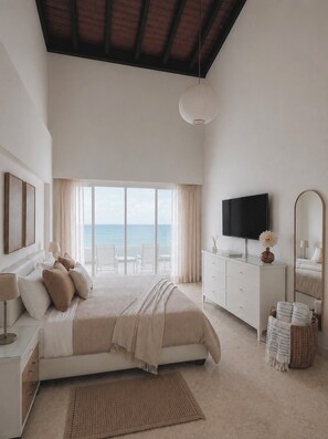 Ein Schlafzimmer mit einem großen Bett, einem Fernseher, einem Schminktisch und Blick auf das Meer.