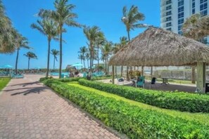 A pathway lined with palm trees and a thatched-roof structure, leading to a pool area. - Home w/2 Queen beds at Tides (Hollywood)