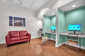 A room with a red leather couch, two desks with computers, a chair, and artwork on the wall. - Home w/2 Queen beds at Tides (Hollywood)