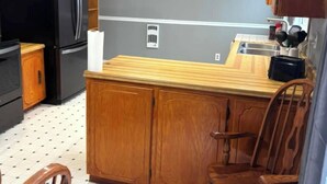 Uma cozinha com armários de madeira, uma geladeira preta, uma mesa de jantar de madeira com cadeiras e piso ladrilhado.