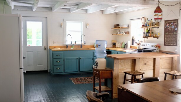 A kitchen with a blue island, wooden cabinets, a water dispenser, and a hanging light fixture. - Cute Modern Farmhouse in Essex, . (Essex)