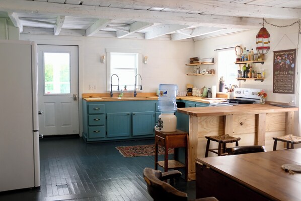 A kitchen with a blue island, wooden cabinets, a water dispenser, and a hanging light fixture.
