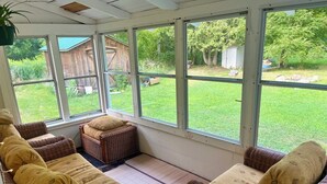 A sunroom with wicker furniture, large windows, and a view of a backyard. - Cute Modern Farmhouse in Essex, . (Essex)