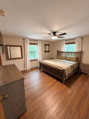 A bedroom with a wooden bed, a ceiling fan, a dresser, and a window with curtains. - Cozy Pocono Getaway - near Shawnee & Bushkill (East Stroudsburg)