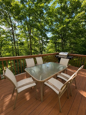 A deck with a glass-top table and wicker chairs, surrounded by a wooden railing, with a grill in the background. - Cozy Pocono Getaway - near Shawnee & Bushkill (East Stroudsburg)