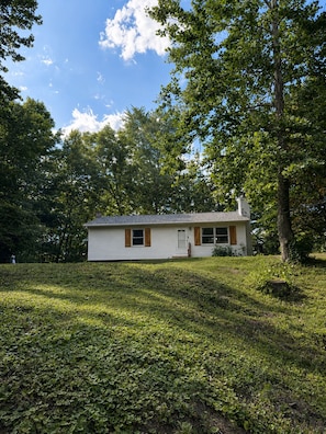 A single-story house with a front porch, surrounded by a well-maintained lawn and trees. - Cozy Pocono Getaway - near Shawnee & Bushkill (East Stroudsburg)