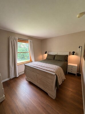 Ein Schlafzimmer mit Bett, Nachttischen, einem Fenster mit Vorhängen und einem Beistelltisch.
