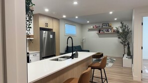 A modern kitchen with a stainless steel refrigerator, a white countertop, and a bar area with stools.