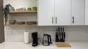 A kitchen with white cabinets, a coffee maker, a kettle, and a knife block.