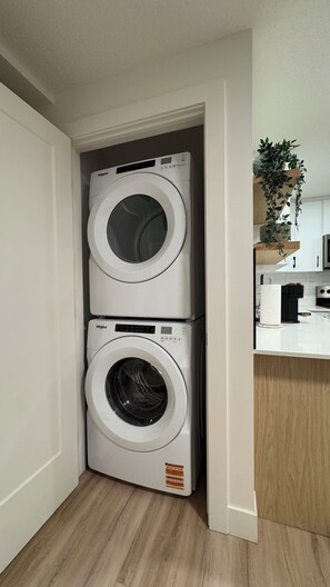 A compact laundry area with two stacked Whirlpool washers, a wooden countertop, and a potted plant.
