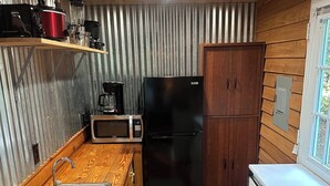 Eine kleine Küche mit Spüle, Mikrowelle, einem schwarzen Kühlschrank und Holzschränken.