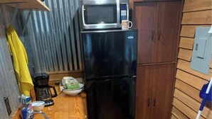 Una cocina compacta equipada con microondas, refrigerador, lavamanos y armarios de madera.