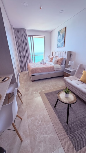 A modern bedroom with a large bed, a sofa, a dining table, and a view of the sea. - 16th floor with panoramic views of the ocean and sunsets (Santa Marta)