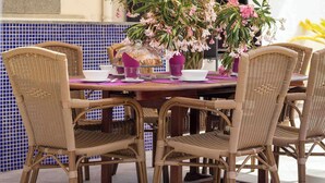 Ein Essbereich im Freien mit Korbstühlen, einem Tisch, der mit rosa Blumen gedeckt ist, und einer gefliesten Rückwand.