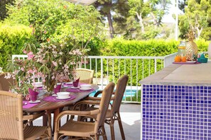 An outdoor dining area with wicker chairs, a wooden table, and a potted plant with pink flowers. - Fantastic villa with pool in Puerto de Alcudia (Port d'Alcúdia)