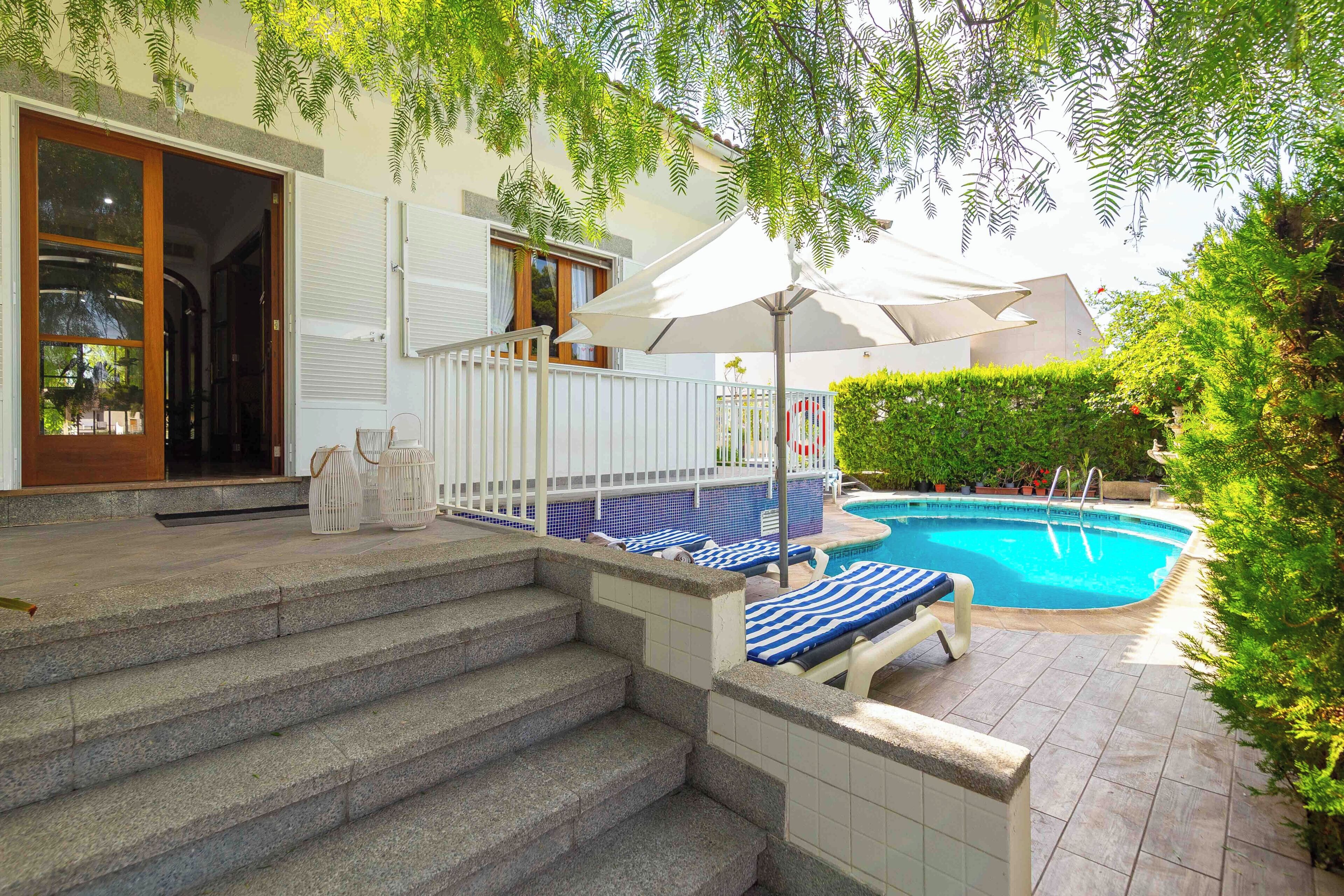 A swimming pool with lounge chairs, a staircase leading to a door, and a white fence.