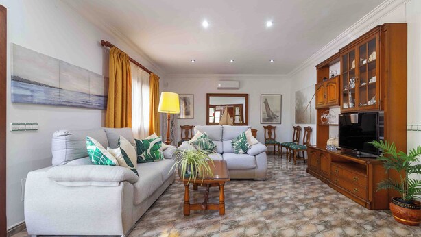 Ein Wohnzimmer mit Sofa, Sesseln, Couchtisch, Fernseher und Schrank.
