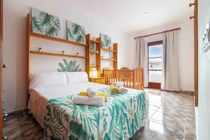 Ein Hotelzimmer mit einem Bett, einem Holzkopfende, einem Nachttisch, einem Sessel, einem Fenster mit Vorhängen und einer Wand mit Pflanzendekorationen.