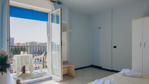 Habitación de hotel con balcón, cama con toallas, armario y una pequeña mesa con una silla.