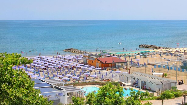 Un resort en la playa con piscina, sombrillas y vista al mar.