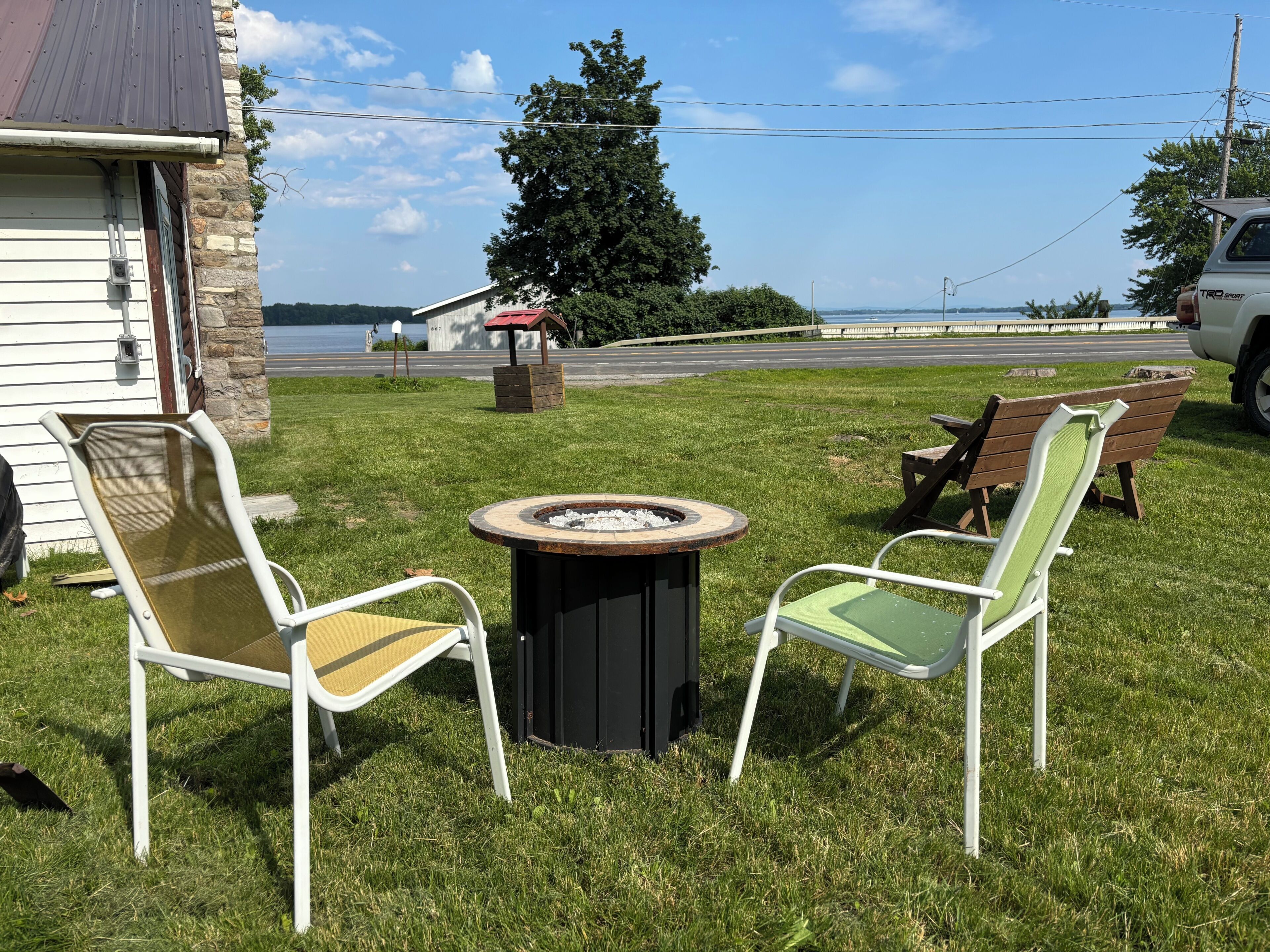 Un espace extérieur verdoyant avec un foyer, deux chaises et un banc.