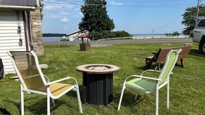 Un espace extérieur verdoyant avec un foyer, deux chaises et un banc.