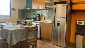 A kitchen with wooden cabinets, a stainless steel refrigerator, a microwave, and a dining table set with plates and glasses.