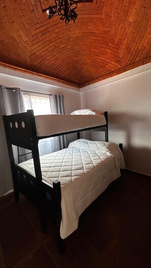 Una cama litera en una habitación con techo de madera y una ventana con cortinas.