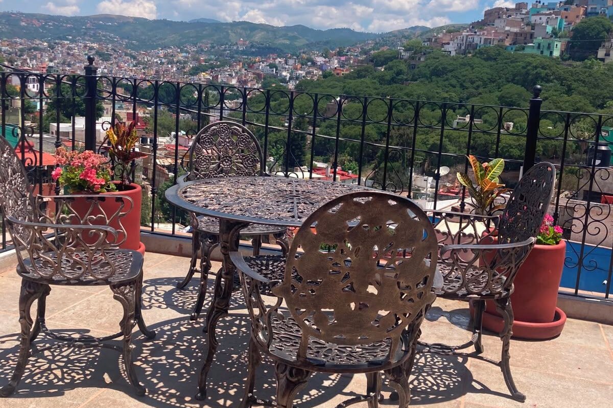 A terrace with a table and chairs, potted plants, and a view of a cityscape.
