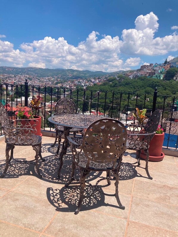 A terrace with a table and chairs, potted plants, and a view of a cityscape.