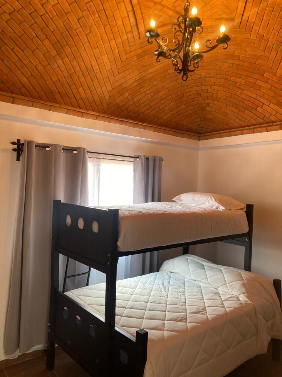 Een kamer met een stapelbed, een kroonluchter en een raam met gordijnen.