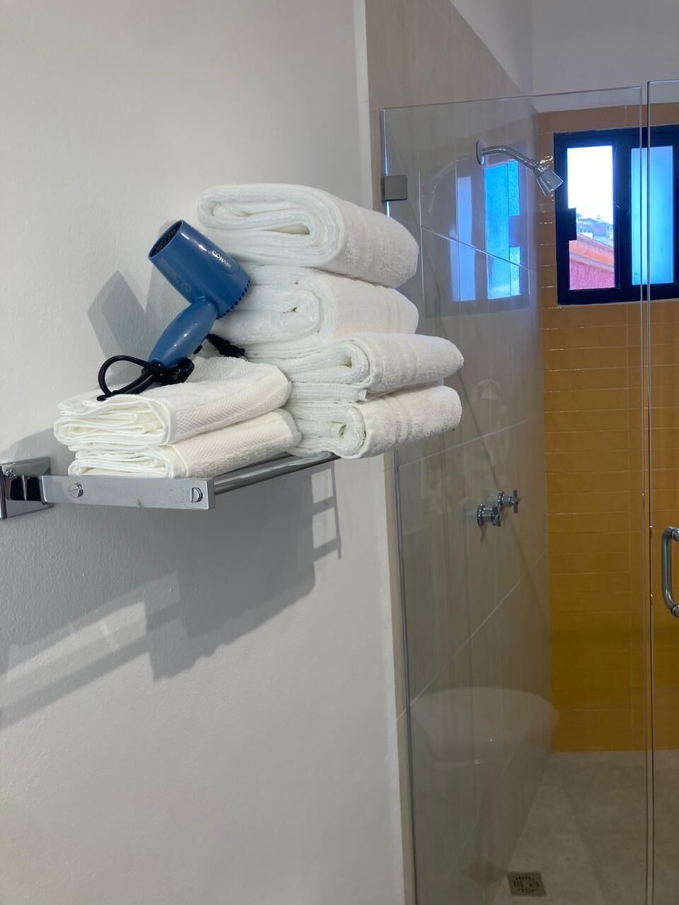 A bathroom with a glass shower enclosure, a towel rack with neatly folded towels, and a hairdryer.